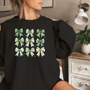 May include: Black sweatshirt with a pattern of green and white shamrock bows. The bows are arranged in a grid pattern.