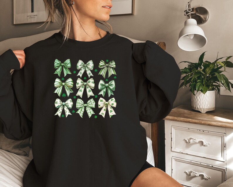 May include: Black sweatshirt with a pattern of green and white shamrock bows. The bows are arranged in a grid pattern.