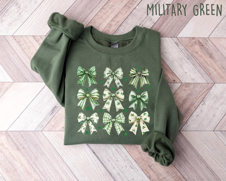 May include: A green sweatshirt with a pattern of green and white bows with shamrock designs. The sweatshirt is labeled "MILITARY GREEN".