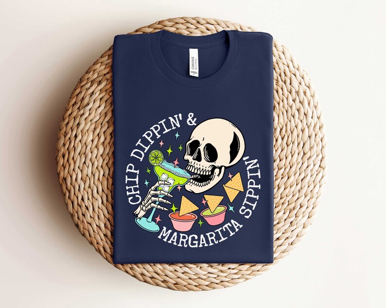 Pu&ograve; includere: Una maglietta blu navy con una grafica bianca di uno scheletro che beve una margarita e intinge patatine. Il testo sulla maglietta recita "Chip Dippin' & Margarita Sippin'."