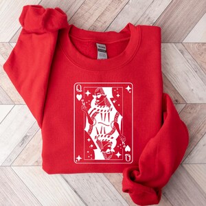 May include: Red sweatshirt with a white graphic of a queen of hearts playing card. The queen is wearing sunglasses and a crown.