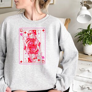 May include: A gray sweatshirt with a pink and red illustration of a queen of hearts playing card. The queen is wearing sunglasses and holding a flower.