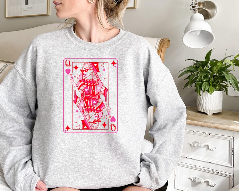 May include: A gray sweatshirt with a pink and red illustration of a queen of hearts playing card. The queen is wearing sunglasses and holding a flower.