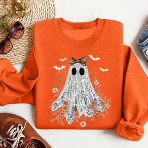 Peut inclure: Sweat-shirt orange avec un fant&ocirc;me blanc portant un n&oelig;ud noir. Le fant&ocirc;me est entour&eacute; de fleurs et de chauves-souris.