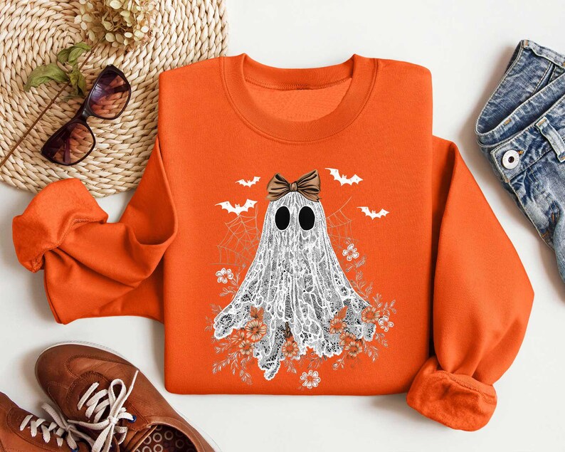 Peut inclure: Sweat-shirt orange avec un fant&ocirc;me blanc portant un n&oelig;ud noir. Le fant&ocirc;me est entour&eacute; de fleurs et de chauves-souris.