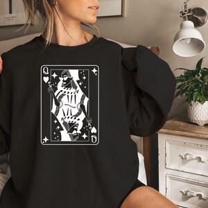 May include: Black sweatshirt with a white graphic of a queen of hearts playing card. The queen is wearing sunglasses and holding a flower.