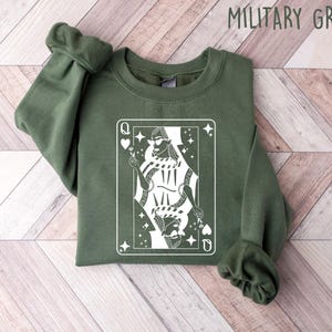 May include: A green sweatshirt with a white graphic of a queen of hearts playing card. The queen is wearing a crown and sunglasses and holding a flower.
