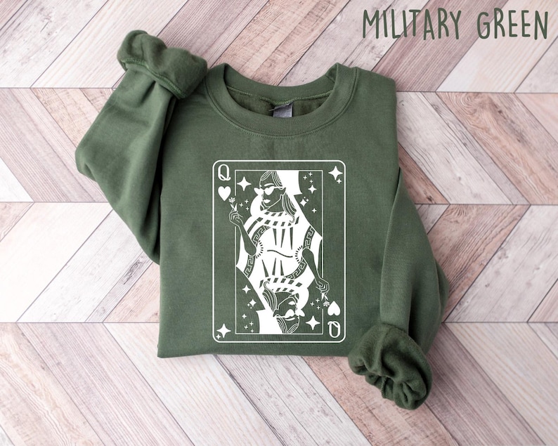 May include: A green sweatshirt with a white graphic of a queen of hearts playing card. The queen is wearing a crown and sunglasses and holding a flower.