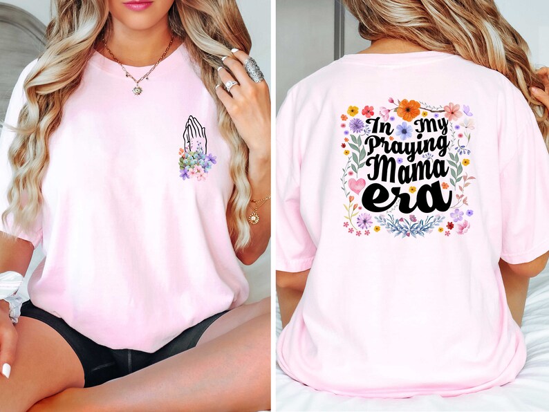 May include: Pink t-shirt with a floral design and the text "In my Praying Mama era" on the back. The front of the shirt has a small design of hands in a praying position with flowers.
