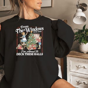 May include: Black sweatshirt with a Christmas-themed graphic. The graphic features a decorated Christmas tree, presents, and two children. Text on the sweatshirt reads "From The Windows To The Walls, I'm About To DECK THESE HALLS."