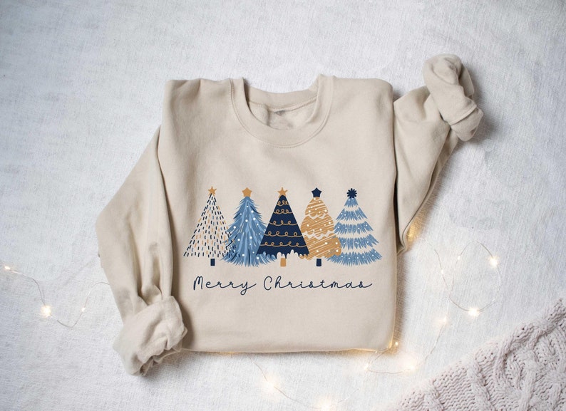 May include: A beige sweatshirt with a graphic of four blue and gold Christmas trees and the text "Merry Christmas".