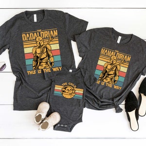 May include: Three gray t-shirts with a retro design featuring a Mandalorian character. The shirts have the text "The Dadalorian", "The Mandalorian", and "The Child" with the phrase "This is the way" on the larger shirts.