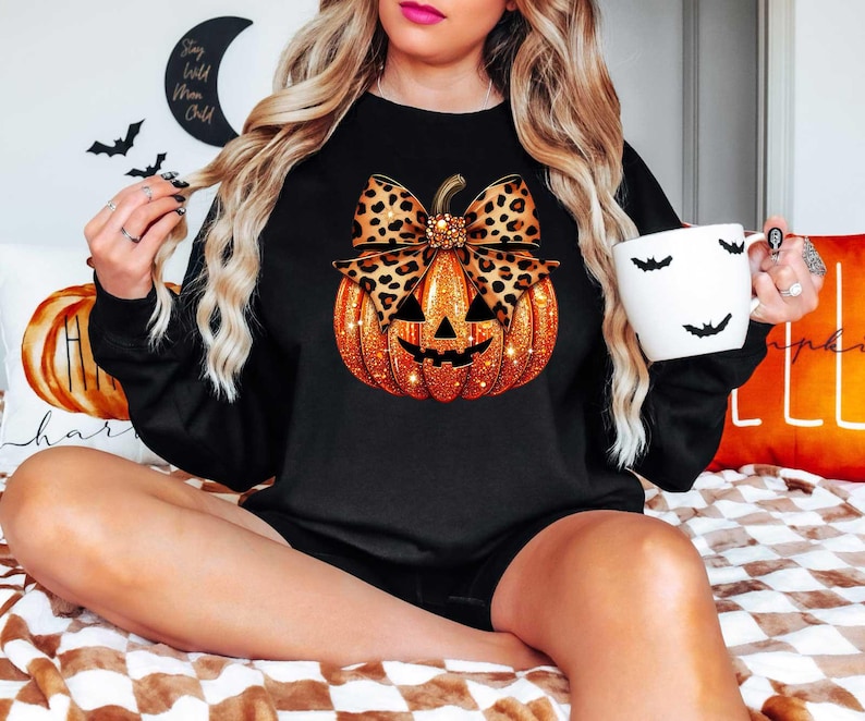 Peut inclure: Sweat-shirt noir avec une citrouille orange scintillante orn&eacute;e d'un n&oelig;ud en imprim&eacute; l&eacute;opard. La citrouille a un visage de citrouille.