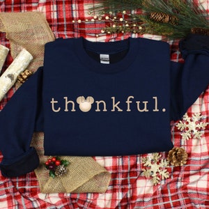 May include: Navy blue sweatshirt with the text "thankful" in beige with a beige Mickey Mouse head with a red bow.