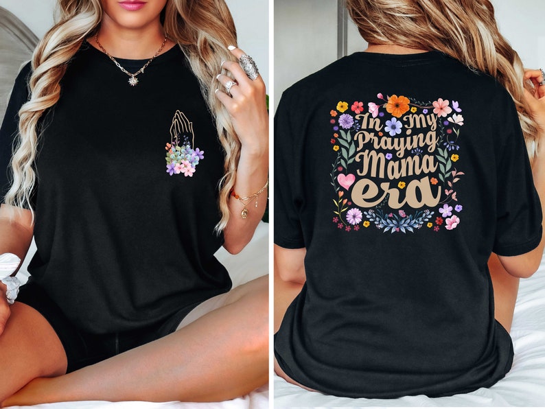 May include: Black t-shirt with a floral design and the text "In my Praying Mama era" on the back. The front of the shirt features a floral design with a praying hand.