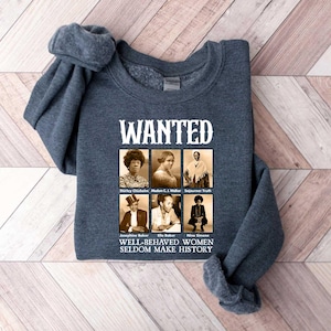 K&ouml;nnte beinhalten: Ein dunkelgraues Sweatshirt mit dem Text "WANTED" in wei&szlig;en Buchstaben. Unter dem Text befinden sich sechs Schwarzwei&szlig;fotos von Frauen mit dem Text "WELL-BEHAVED WOMEN SELDOM MAKE HISTORY" unter den Fotos.