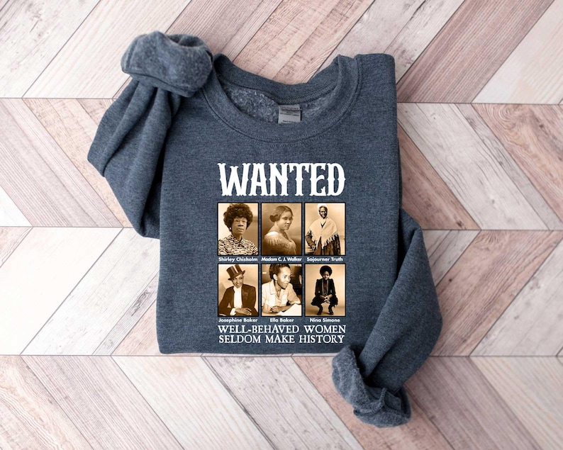 K&ouml;nnte beinhalten: Ein dunkelgraues Sweatshirt mit dem Text "WANTED" in wei&szlig;en Buchstaben. Unter dem Text befinden sich sechs Schwarzwei&szlig;fotos von Frauen mit dem Text "WELL-BEHAVED WOMEN SELDOM MAKE HISTORY" unter den Fotos.