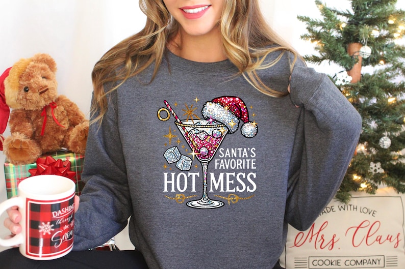 May include: A gray sweatshirt with a sparkly design of a martini glass with a Santa hat on top. The text "Santa's Favorite Hot Mess" is printed below the glass.