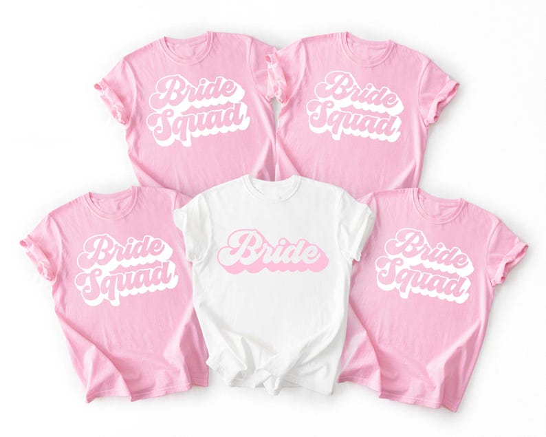 May include: Five t-shirts, four pink and one white, with the words "Bride Squad" and "Bride" in a retro font. The pink shirts have "Bride Squad" in white and pink, while the white shirt has "Bride" in pink.