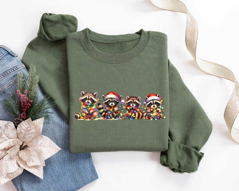May include: A green sweatshirt with a Christmas-themed design featuring five raccoons wearing Santa hats and holding Christmas lights.