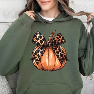 May include: A green hoodie with a pumpkin design. The pumpkin has a leopard print bow on top.