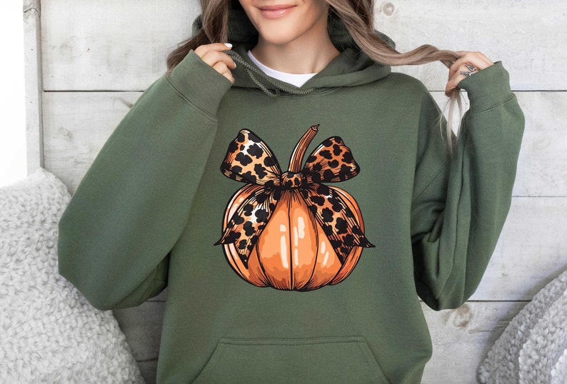 May include: A green hoodie with a pumpkin design. The pumpkin has a leopard print bow on top.