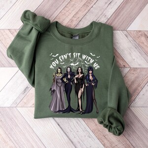 May include: Green sweatshirt with a white graphic of three women in black dresses and the text "You can't sit with us".