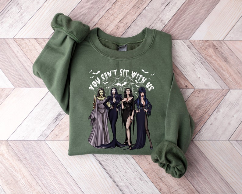 May include: Green sweatshirt with a white graphic of three women in black dresses and the text "You can't sit with us".