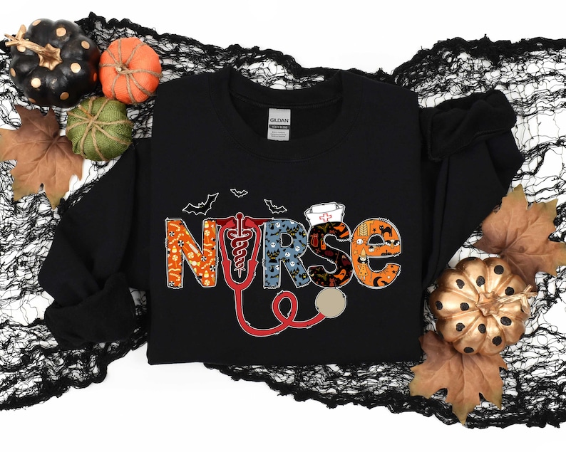 Pu&ograve; includere: Felpa nera con una grafica "NURSE" a tema Halloween. Le lettere sono composte da varie icone di Halloween, tra cui pipistrelli, fantasmi, zucche e mais caramellato. Un stetoscopio rosso &egrave; incluso nel design.