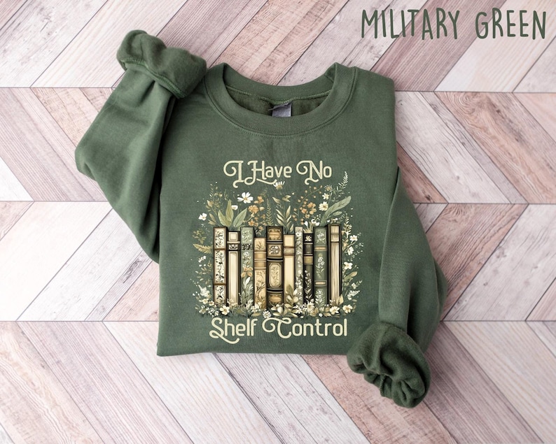 May include: Military green sweatshirt with the text "I Have No Shelf Control" and a graphic of vintage books surrounded by floral elements. The long-sleeved crew neck top is made of a soft material.