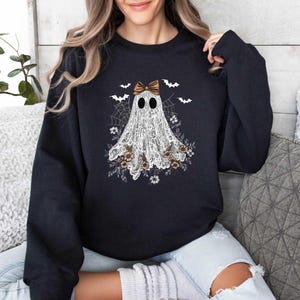 Peut inclure: Sweat-shirt noir avec un fant&ocirc;me blanc portant un n&oelig;ud brun. Le fant&ocirc;me est entour&eacute; de d&eacute;tails floraux et de chauves-souris.