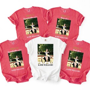May include: Red and white t-shirts with a photo of a person in a graduation gown. The red shirts say "Proud Grandmother of a," "Proud Mom of a," "Proud Grandfather of a," and "Proud Dad of a." The white shirt says "2026 KATE WILLIAMS."