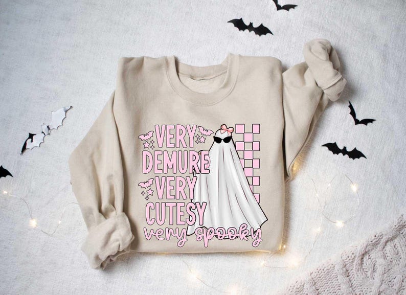 May include: A beige sweatshirt with a pink and white graphic of a ghost with the text "Very Demure Very Cutesy Very Spooky".