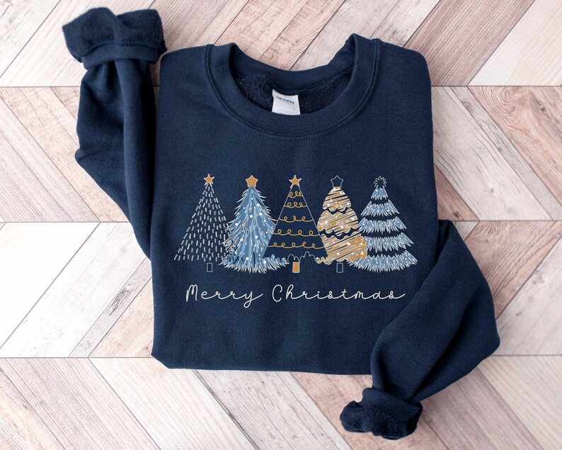 May include: A navy blue sweatshirt featuring a festive design of five stylised Christmas trees in gold and blue with the text "Merry Christmas" underneath.
