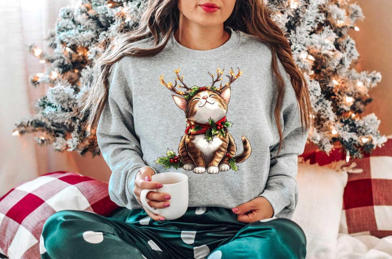 May include: A gray sweatshirt with a cute cartoon cat wearing a reindeer antler headband. The cat is brown and white with green holly and red berries around its neck. The cat is smiling and has a happy expression.