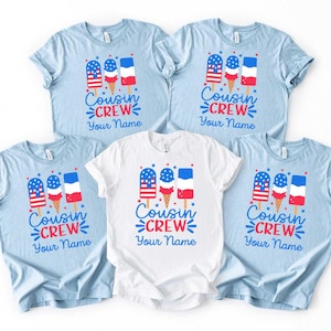 May include: Five light blue and white t-shirts with a popsicle graphic in red, white, and blue. The text "Cousin Crew" and "Your Name" are printed on the front of the shirts. The shirts are short-sleeved.