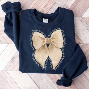May include: Navy blue sweatshirt with a large beige bow graphic and the text "Thankful Grateful Blessed" repeated around the bow.