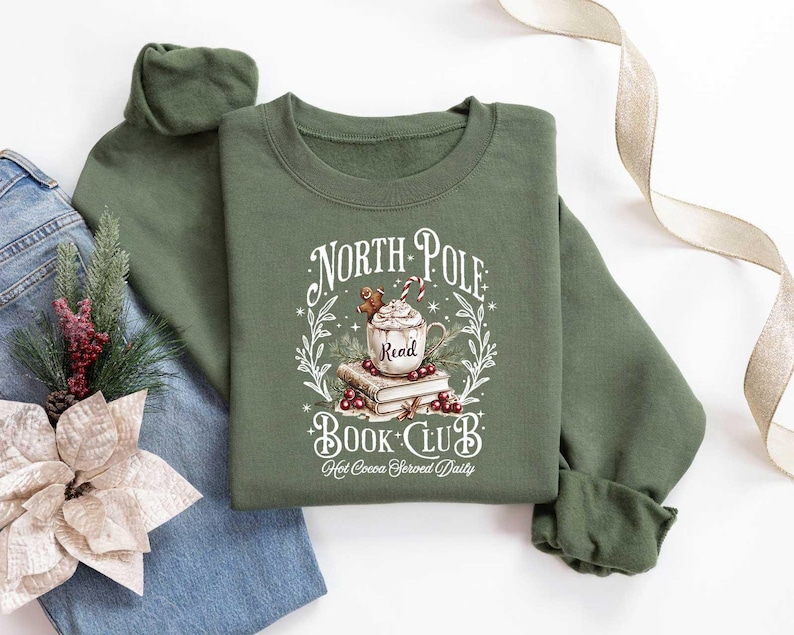 May include: Green sweatshirt with a white graphic design that says "North Pole Book Club" with a mug of hot cocoa and a gingerbread man. The text below the graphic says "Hot Cocoa Served Daily".
