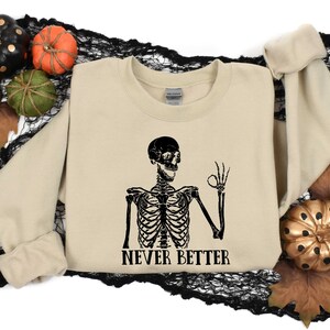 May include: A tan sweatshirt with a black skeleton graphic and the text "NEVER BETTER".
