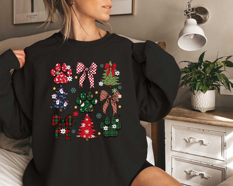 May include: Black sweatshirt with a Christmas-themed design featuring paw prints, bows, and Christmas trees. The design is in red, green, and white.