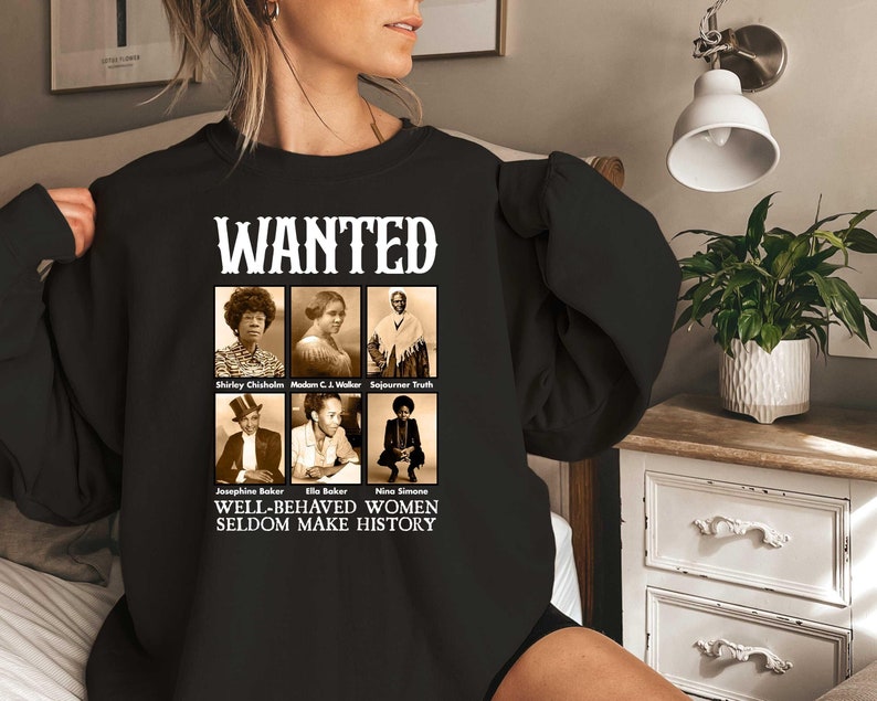 K&ouml;nnte beinhalten: Schwarzer Pullover mit einem wei&szlig;en Grafikdruck eines Fahndungsplakats mit Portr&auml;ts einflussreicher Frauen. Der Text lautet "WANTED" und "WELL-BEHAVED WOMEN SELDOM MAKE HISTORY".