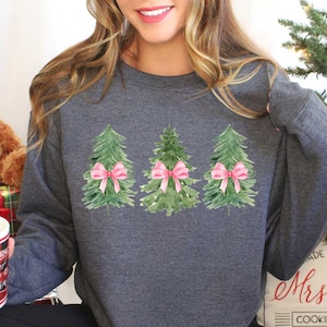 May include: A gray sweatshirt with a design of three watercolor Christmas trees with pink bows. The text "Mrs. Claus Cookie Company" is on the bottom of the sweatshirt.