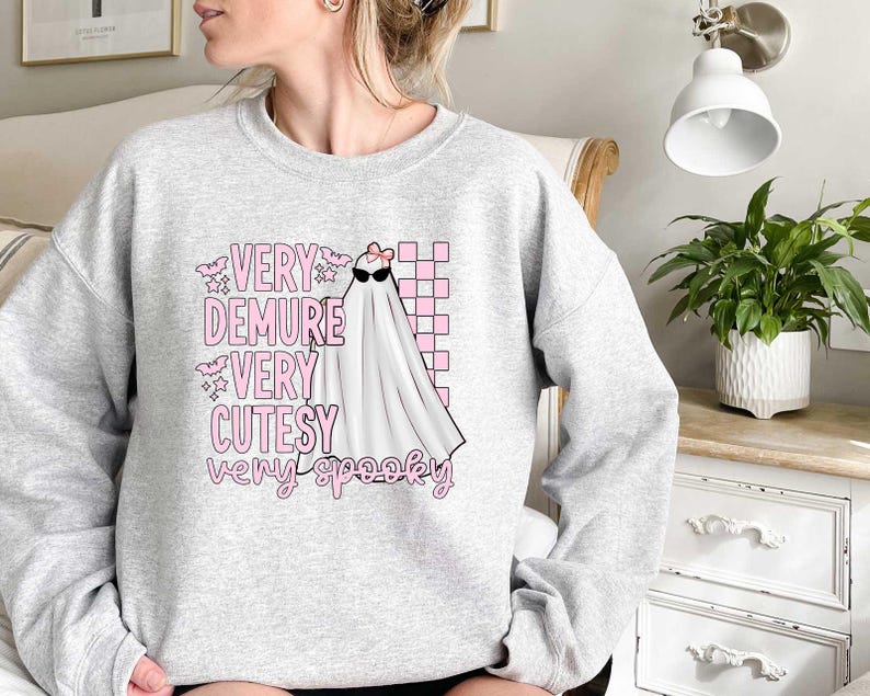 May include: A gray sweatshirt with a pink and white graphic of a ghost wearing sunglasses and a bow. The text on the sweatshirt reads "Very Demure Very Cutesy Very Spooky."