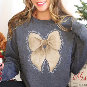 May include: A gray sweatshirt with a large beige bow design. The bow is surrounded by the words "Thankful, Grateful, Blessed" repeated in a circle.