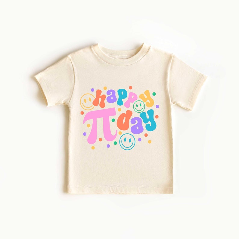 May include: A cream-coloured t-shirt with a colourful graphic that says "happy pi day" with a pink pi symbol and smiley faces.