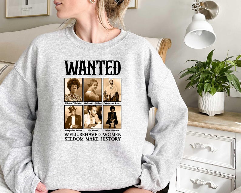 K&ouml;nnte beinhalten: Grauer Pullover mit einem Grafikdruck eines Fahndungsplakats mit Schwarzwei&szlig;fotos von bemerkenswerten Frauen. Der Text auf dem Plakat lautet "WANTED" und "WELL-BEHAVED WOMEN SELDOM MAKE HISTORY".