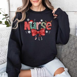 May include: Black sweatshirt with a festive Christmas-themed design that says "Nurse" in colorful letters with a red bow and a stethoscope.