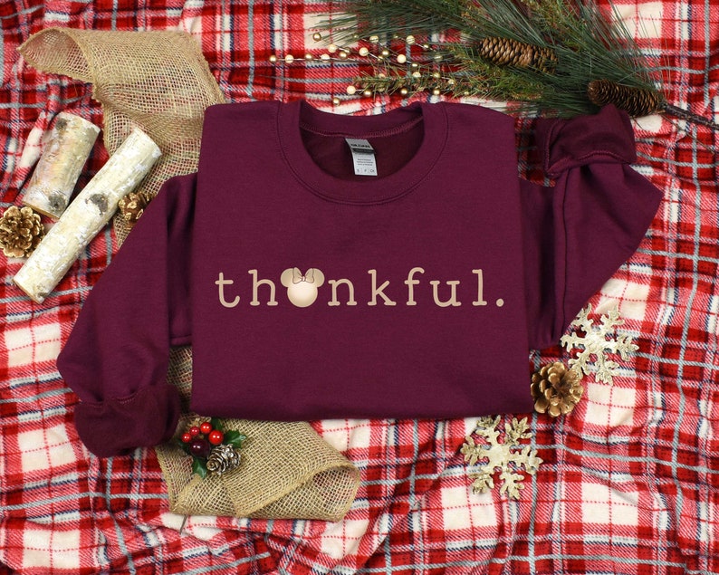 May include: Burgundy sweatshirt with the text "thankful." in a light brown color. A small brown mouse head with a pink bow is in front of the "h" in the word "thankful."