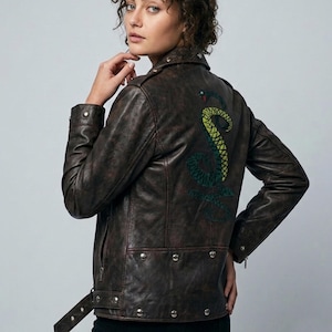 Può includere: Giacca in pelle marrone con un design trapuntato e un serpente ricamato decorativo sul retro. La giacca ha un classico stile biker con colletto a revers, chiusure a scatto e cintura in vita.