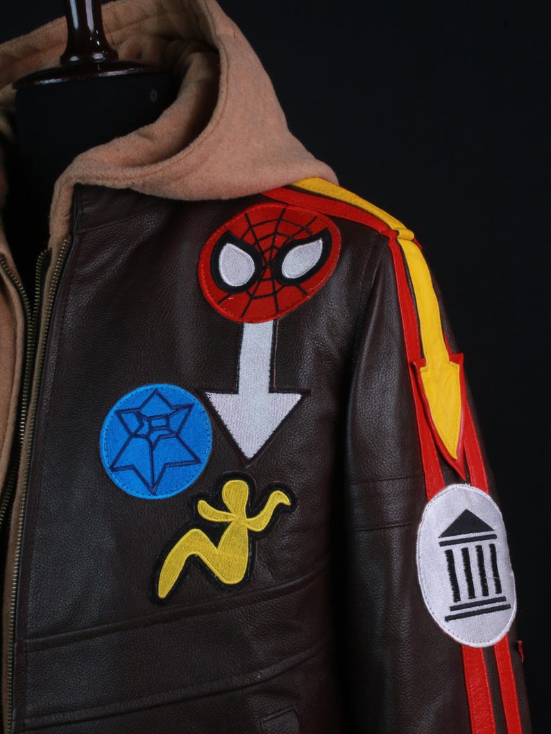 K&ouml;nnte beinhalten: Braune Lederjacke mit beigefarbener Kapuze und mehreren bunten Aufn&auml;hern. Aufn&auml;her sind ein Spider-Man-Logo, ein blauer Stern, eine gelbe Figur und ein wei&szlig;er Pfeil. Rote und gelbe Streifen zieren die Schulter.